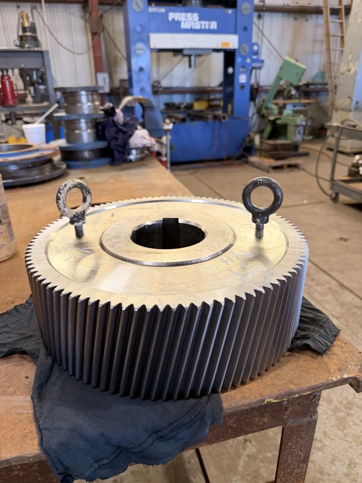 Large helical gear on a workbench with lifting eyes installed.